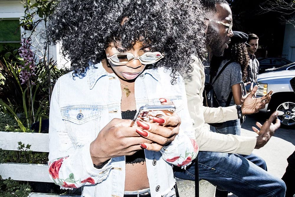 Person with an afro, sunglasses, and red nail polish looking at their phone